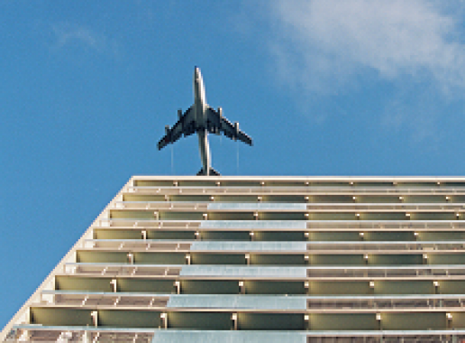 Vliegtuig over flatgebouw van onderaf gezien