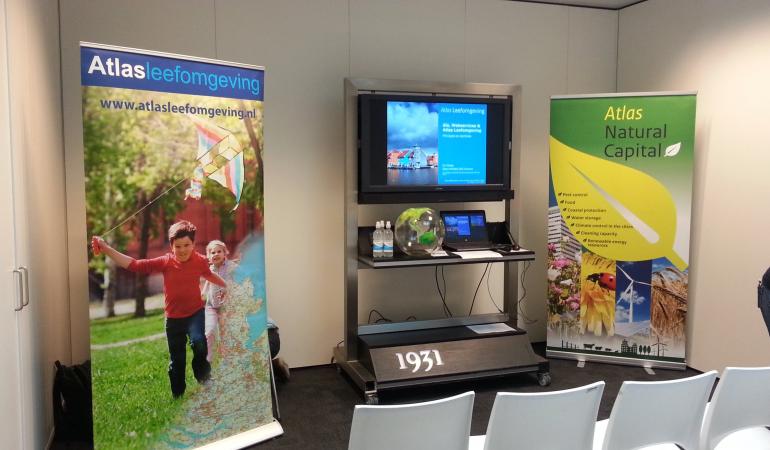 Banners Atlas Leefomgeving en Atlas Natuurlijk Kapitaal en scherm met daarop Atlas Leefomgeving