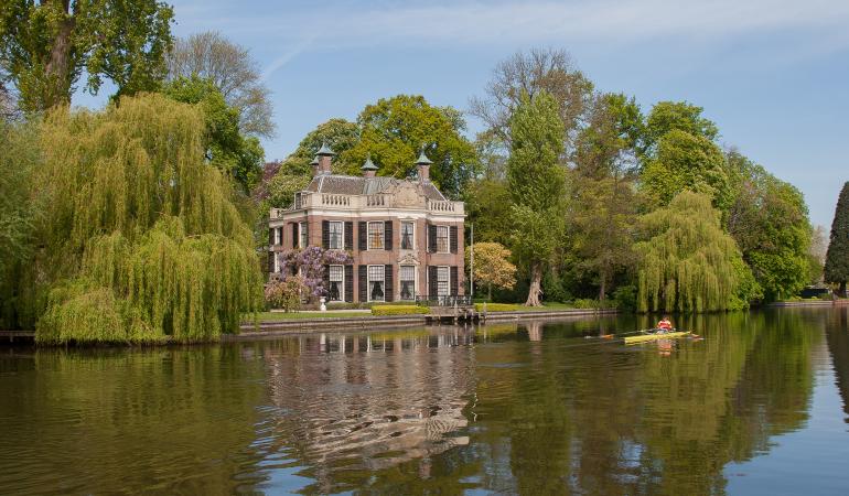 Buitenplaats Zicht vanaf het water op een buitenplaats gelegen aan de oever.