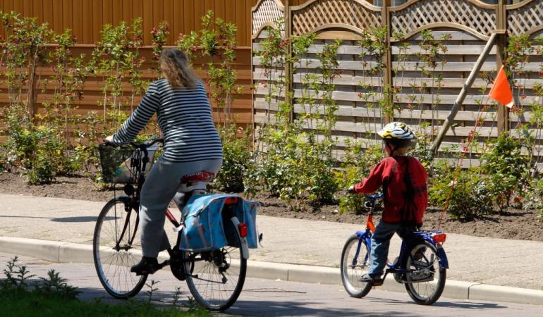 Op de fiets in een woonwijk Moeder en kind op de fiets door een straat in een woonwijk