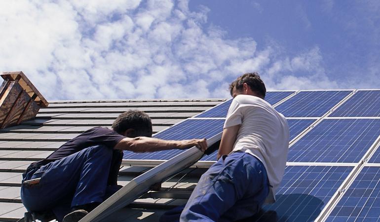 Twee installateurs plaatsen zonnepanelen op een dak tijdens zonnig weer