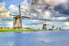 Kinderdijk. Langs de rivier staan vijf molens. Wolkenlucht op de achtergrond