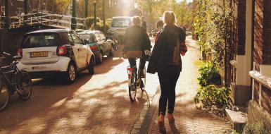 Fietsers, wandelaars en geparkeerde auto's in straat in Leiden in schemering Fietsers, wandelaars en geparkeerde auto's in straat in Leiden in schemering
